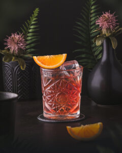East India Negroni - Red Cocktail with an orange wedge garnish.