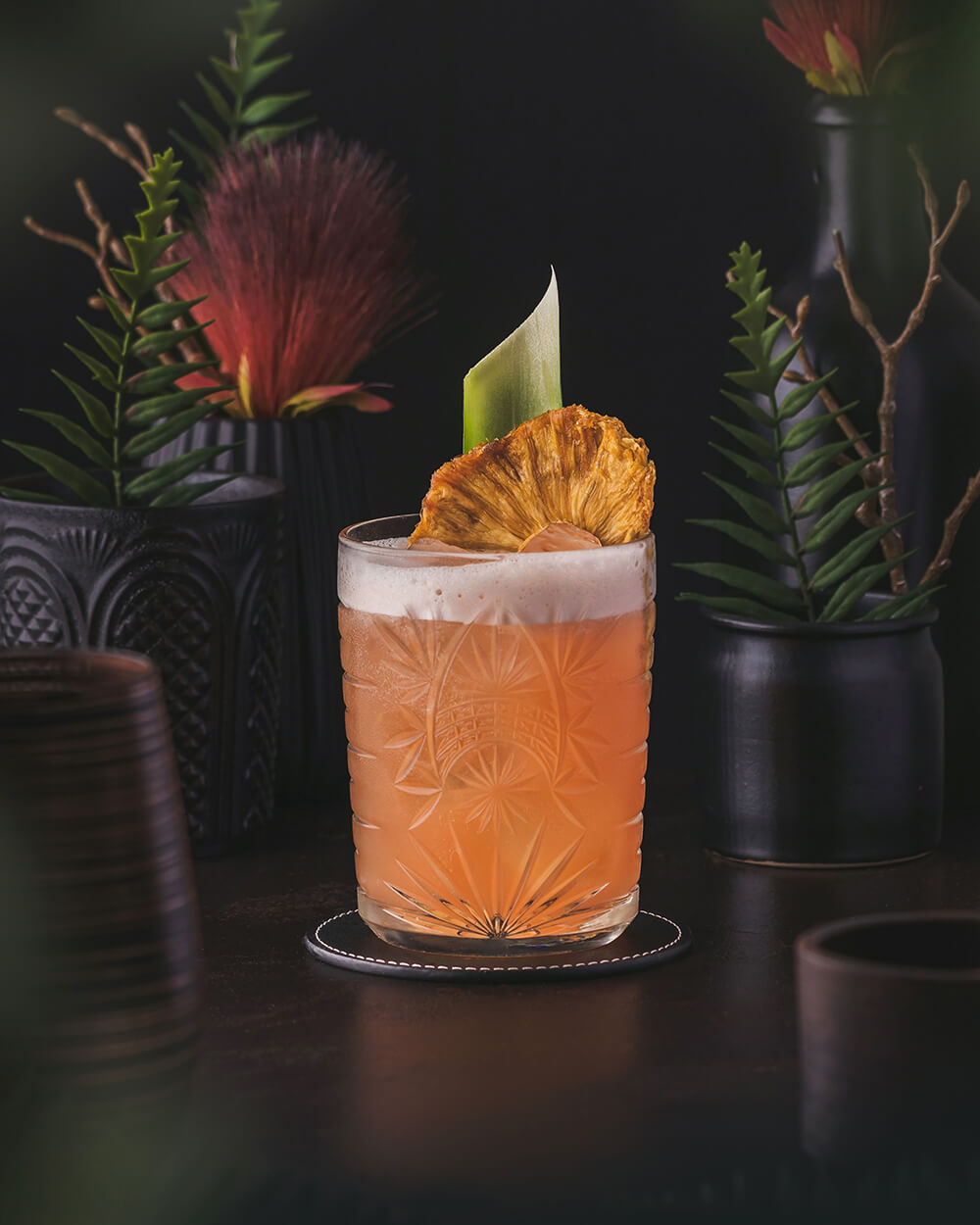 Jungle Bird Cocktail - An interesting orange red colored tiki cocktail that combines Jamaican rum with Campari and pineapple. Garnished with pineapple leaf and pineapple chunks.