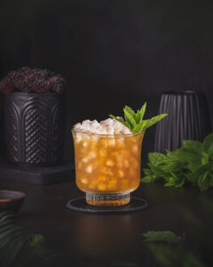 A Dark orange whiskey based cocktail garnished with a sprig of mint. A whiskey sour twist with fernet branca.